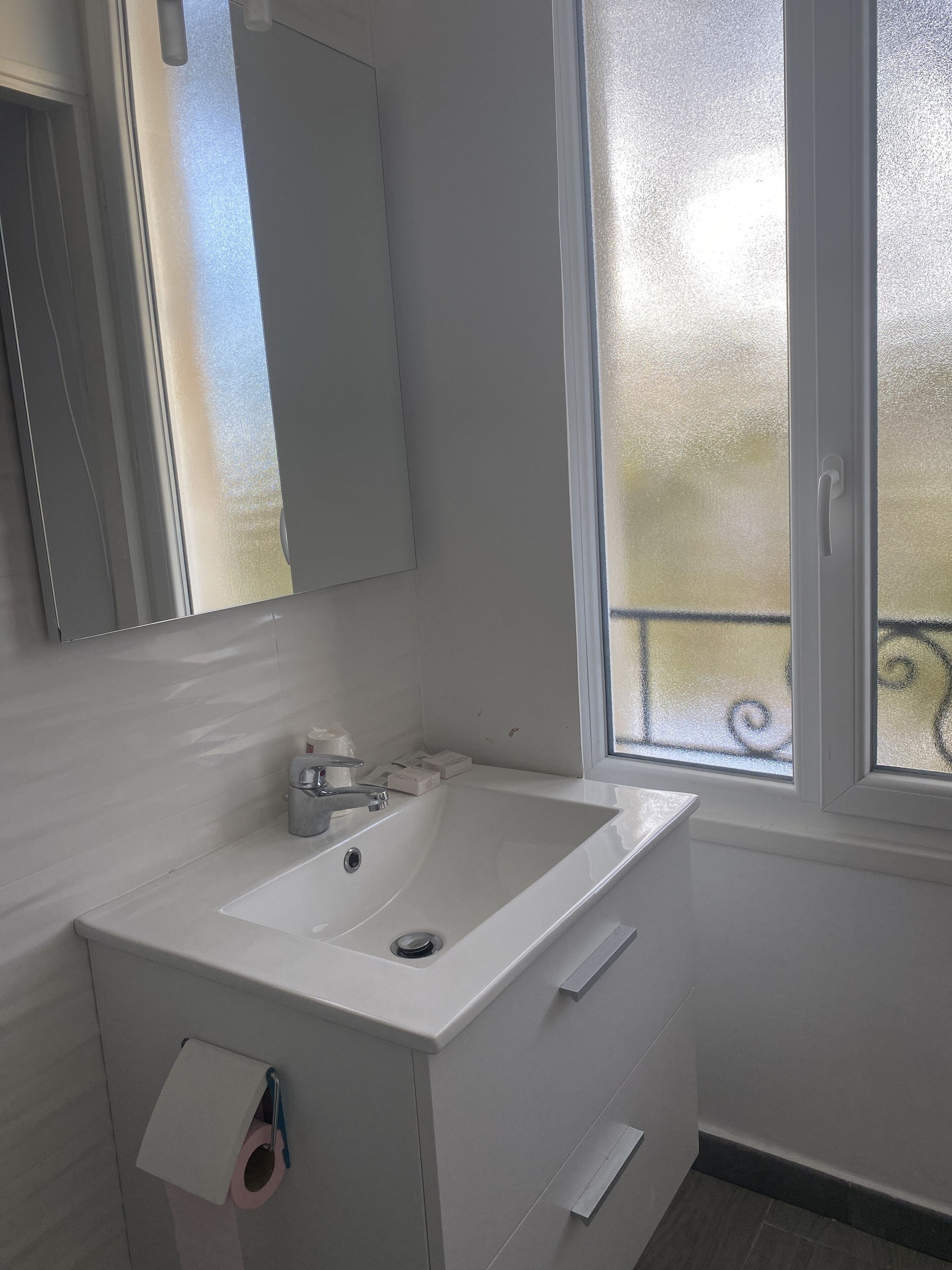 Un baño con lavamanos blanco, espejo y ventana con vista a un balcón.