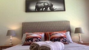 A neatly made bed with two pillows, a rolled towel, and a framed picture of rhinos on the wall above.