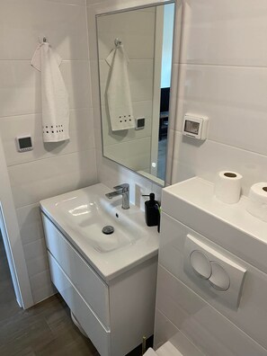 Une salle de bain moderne avec un lavabo blanc, un miroir, des toilettes et un porte-serviettes.