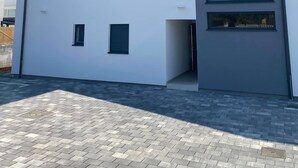 Un edificio moderno con fachada plana, múltiples ventanas y un área de entrada pavimentada.