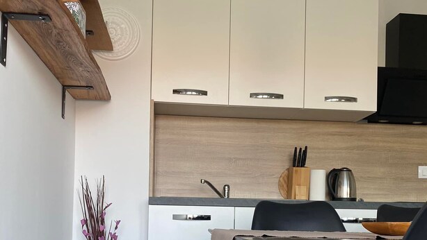 Cocina moderna con armarios blancos, encimera de madera y comedor con una silla y mesa negros.