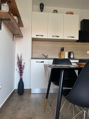 Et moderne køkken med hvide skabe, en træbordplade og et spiseområde med en sort stol og et bord.