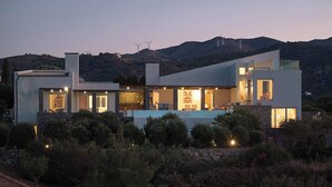 Une maison moderne à deux étages, dotée de grandes fenêtres, d’une piscine et offrant une vue sur des éoliennes en arrière-plan.