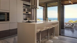 Une cuisine moderne dotée d’un grand îlot central, de tabourets de bar et offrant une vue sur l’océan.