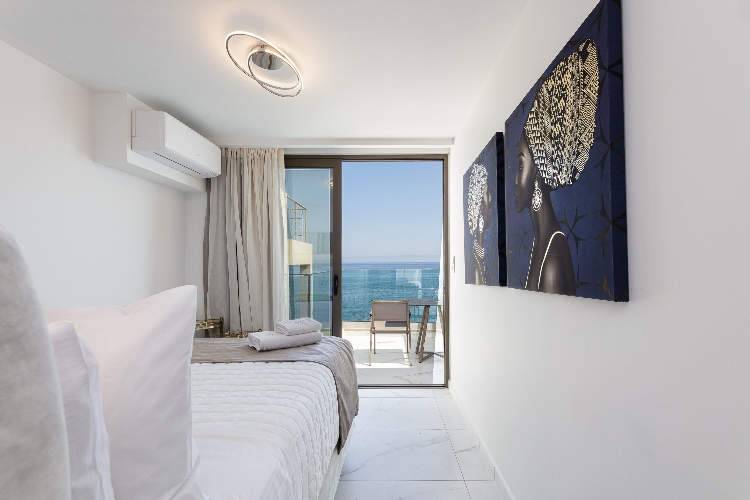 A modern hotel room with a balcony, a bed, a painting, and a view of the sea.