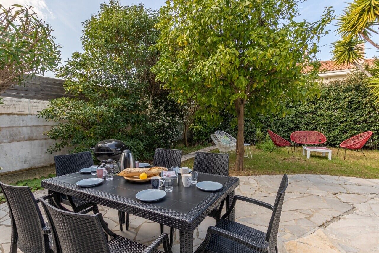 An outdoor patio with a table set for dining, surrounded by wicker chairs and red chairs.