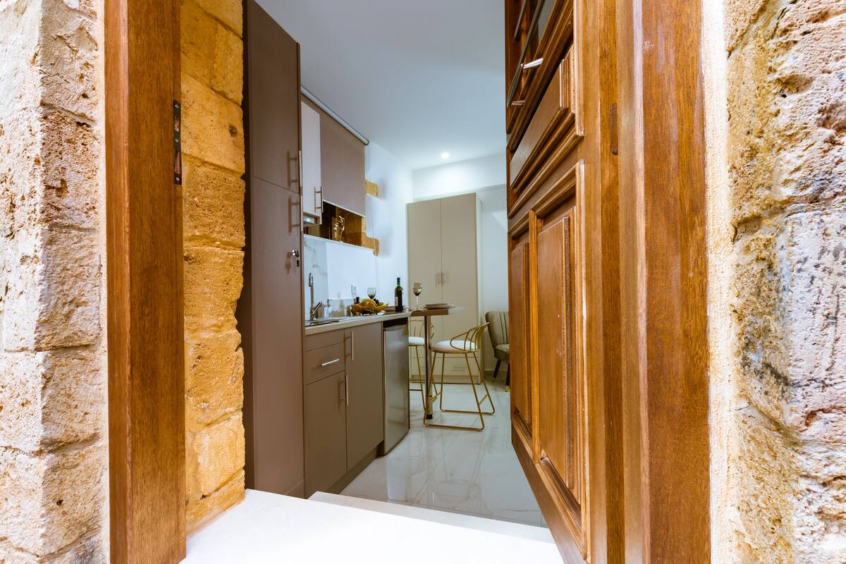 Un pasillo estrecho con una zona de cocina a la izquierda, que incluye armarios y una encimera con una botella de vino y copas.