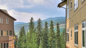 A multi-story building with a stone base and wooden upper floors, surrounded by dense forest and mountains in the background. - Luxurious 2 Br In River Run Village With Ski In Ski Out, No Cleaning Fees, Kids Ski Free 2 Bedroom Condo by RedAwning (Keystone)