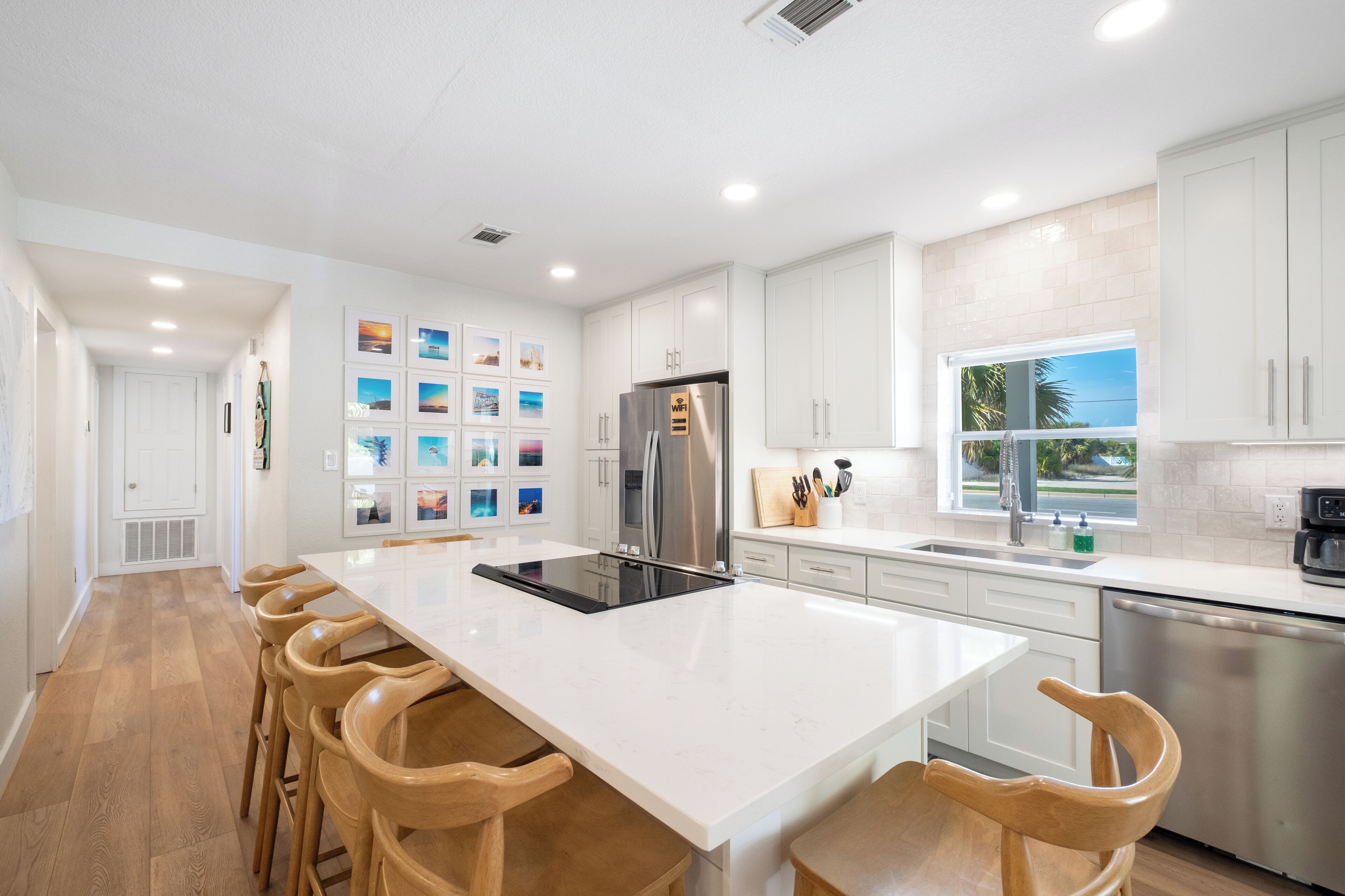 A modern kitchen with a large island, white cabinetry, stainless steel appliances, and a view of the outdoors.