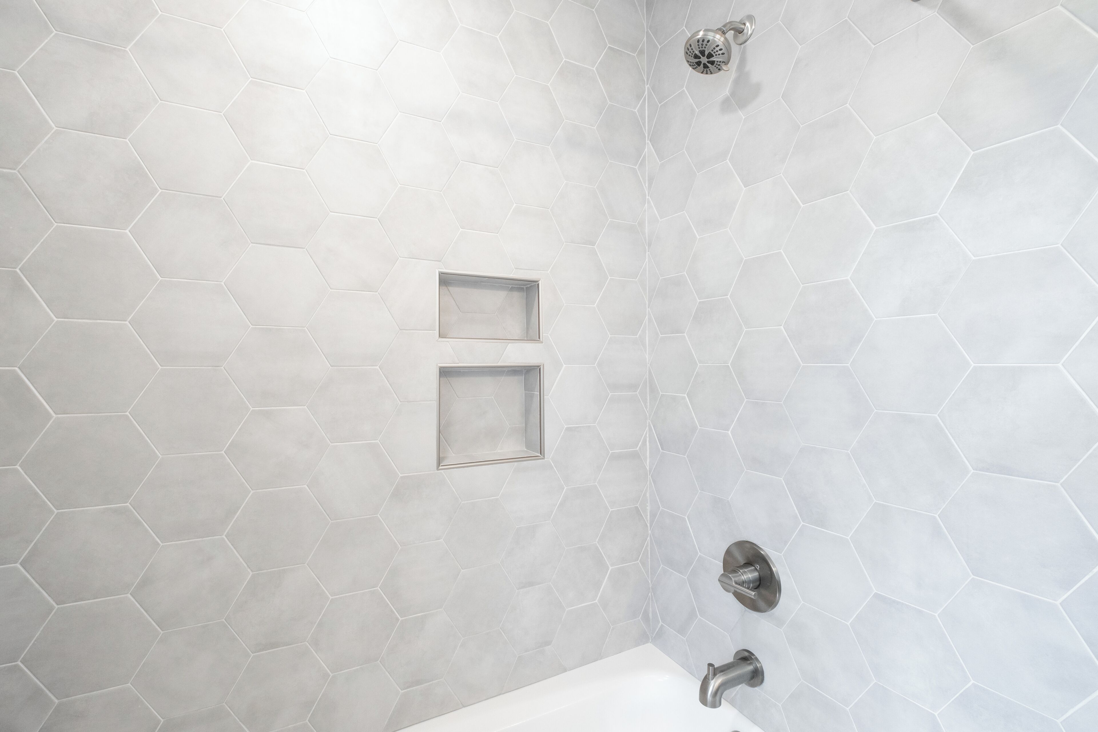 Een badkamer met wandtegels in een honingraatpatroon, een douche en een wastafel.