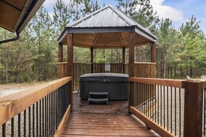 Relax in a serene gazebo with a hot tub, surrounded by tall trees.