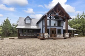 Une maison à deux étages, avec des fondations en pierre, de grandes fenêtres et une terrasse en bois.