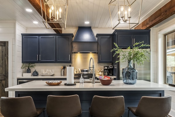 Une cuisine moderne avec des meubles de couleur sombre, un grand îlot central et des luminaires suspendus.