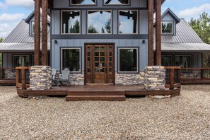 A two-story house with a stone facade, large windows, and a wooden deck. - Geauxin' All Inn -Gameroom, Bunks, Spacious Covered Deck, Paved Rd, Hot Tub (Broken Bow)