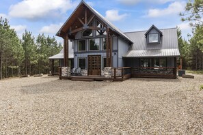 Situated in a forested area, this lodge features a large porch and a mix of large windows.