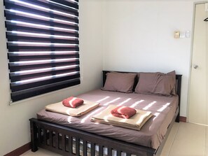 A bedroom with a bed, pillows, a bedside table, and a window with blinds. - OYO 90476 Casa Azlinda Muslim Homestay I (Johor Bahru)
