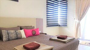 Habitación de hotel con una cama grande, dos almohadas, una ventana con persianas y vistas al exterior.