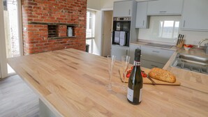 A kitchen with a brick fireplace, wooden countertop, wine bottle, glasses, and a loaf of bread. - Shippon (York)
