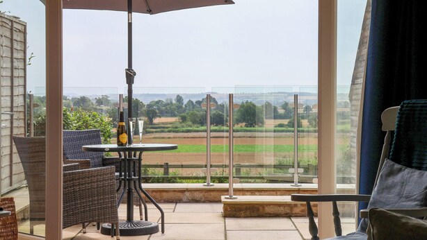 A balcony with a table, chairs, and an umbrella, overlooking a rural landscape. - Shippon (York)