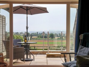A balcony with a table, chairs, and an umbrella, overlooking a rural landscape. - Shippon (York)