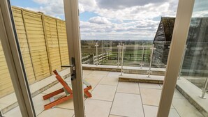 A balcony with a glass door, a wooden chair, and a view of a rural landscape. - Shippon (York)