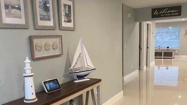 Un couloir avec une console sur laquelle sont disposés un phare blanc, une tablette et une maquette de petit voilier. Des tableaux encadrés ornent le mur, et une pancarte « Bienvenue chez nous » est accrochée au-dessus d’une porte.
