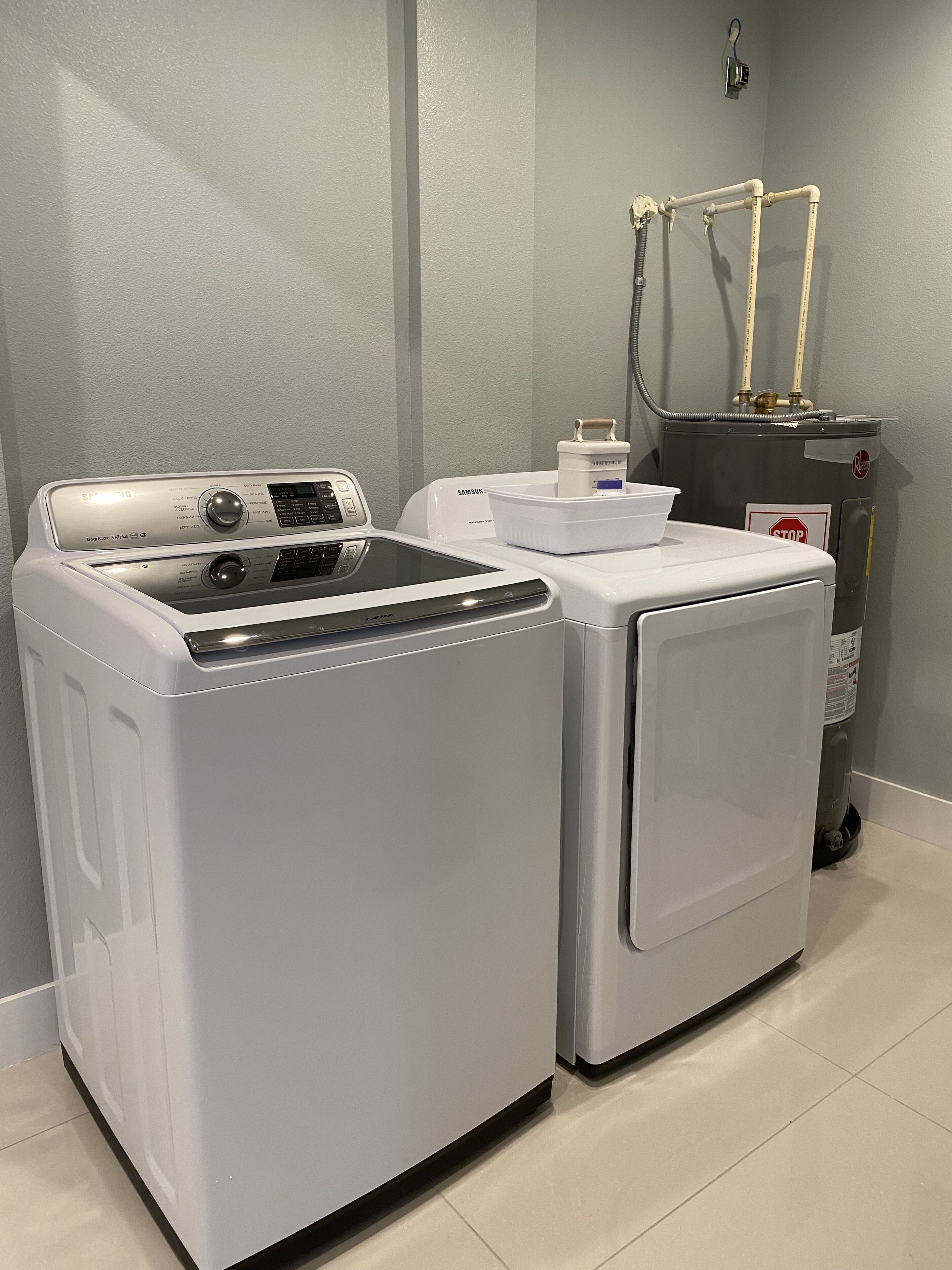 A laundry room with a front-loading washer and dryer, a water heater, and a hose.
