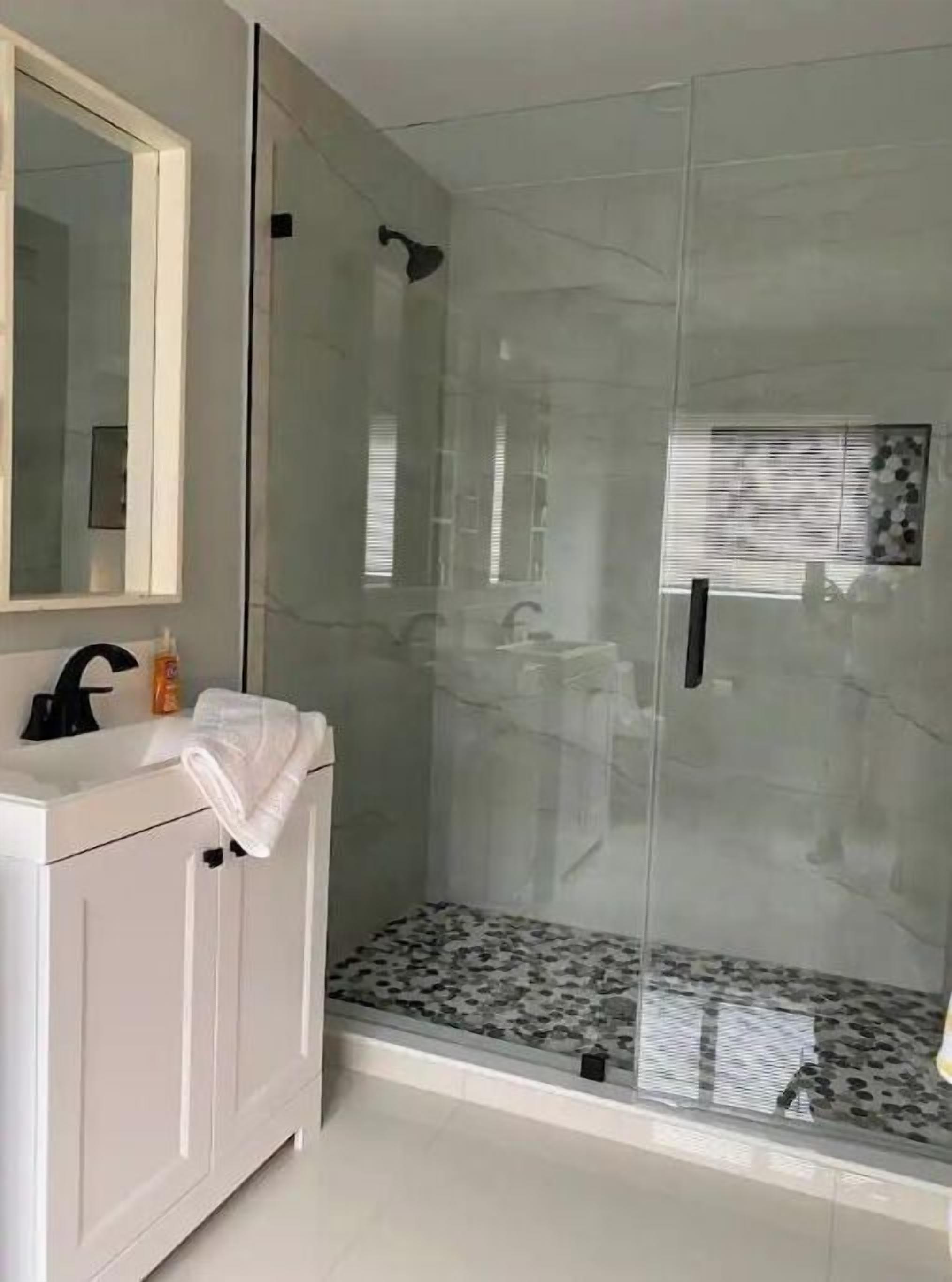 A bathroom with a glass-enclosed shower, a white vanity with a mirror, and a tiled floor.