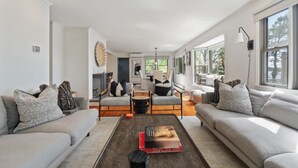 A modern living room with a sofa, armchairs, a coffee table, and a fireplace. - 2 Acre Waterfront Home Overlooking Waquoit Bay with Spa and Swim Dock  (Falmouth)