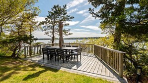 A wooden deck with a table and chairs, overlooking a body of water and surrounded by trees. - 2 Acre Waterfront Home Overlooking Waquoit Bay with Spa and Swim Dock  (Falmouth)