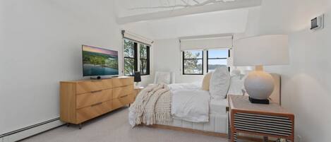 A modern bedroom with a bed, a wooden dresser, a TV, and a lamp.