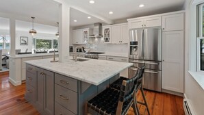 A modern kitchen with white cabinetry, stainless steel appliances, and a marble island. - 2 Acre Waterfront Home Overlooking Waquoit Bay with Spa and Swim Dock  (Falmouth)