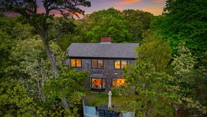 A two-story house with a stone facade, a visible chimney, and a deck with outdoor furniture. - 2 Acre Waterfront Home Overlooking Waquoit Bay with Spa and Swim Dock  (Falmouth)