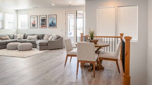 A modern living room with a sectional sofa, a dining table with chairs, and a staircase with a railing. - The Sol Mate: Desert Color Lagoon + Beaches (St George)