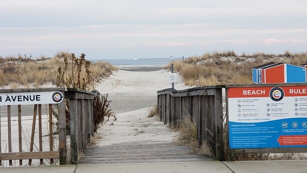Ein Zugang zum Strand mit einem hölzernen Steg, der zum Strand führt, einem Schild mit der Aufschrift 'Miami Avenue' und einem Schild mit Strandregeln und Richtlinien.