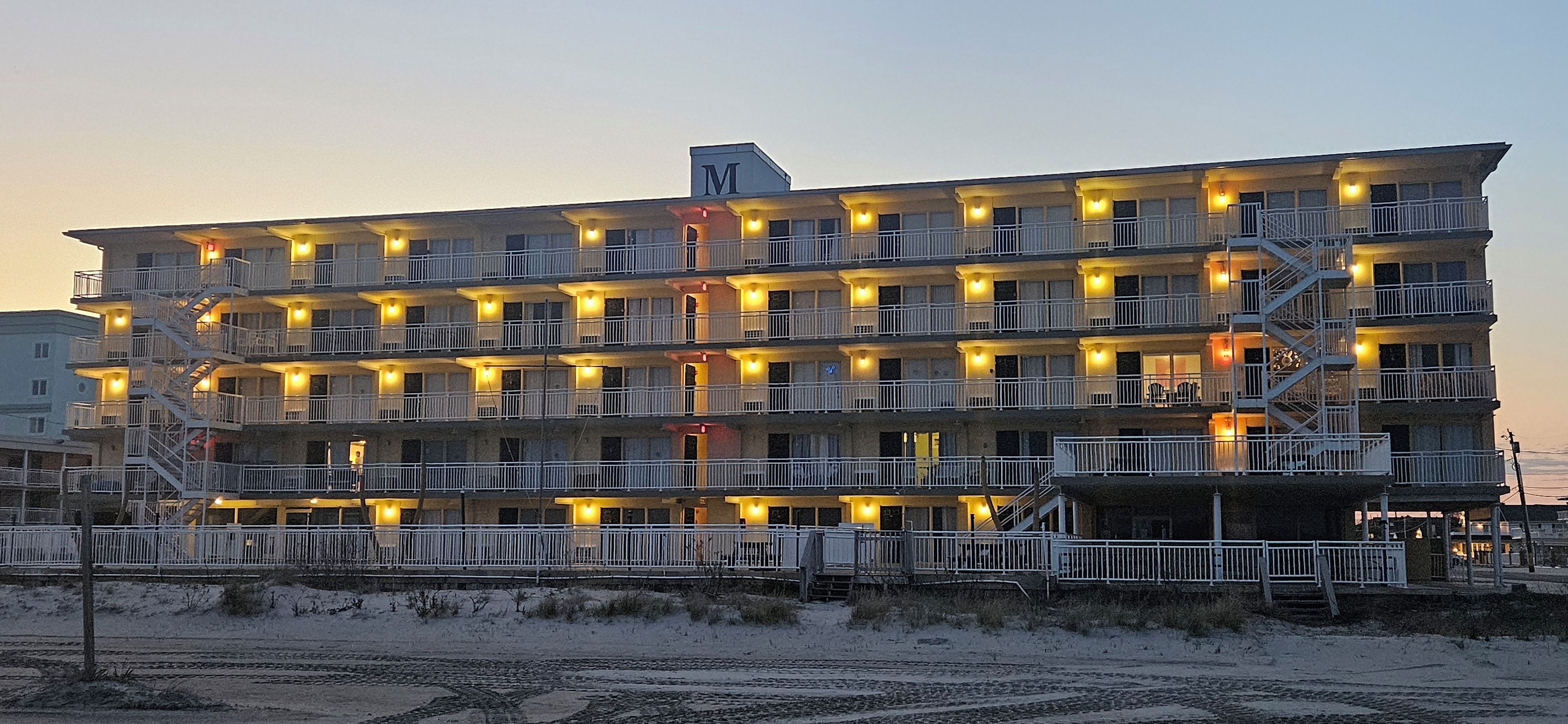 A multi-story hotel with balconies, a fire escape, and a beach view.