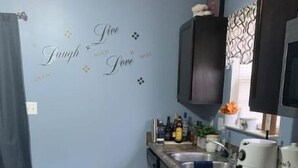 Eine kompakte Küche mit blauer Wand, Holzboden, einer Edelstahl-Spüle und einem schwarzen Schrank über der Arbeitsplatte.