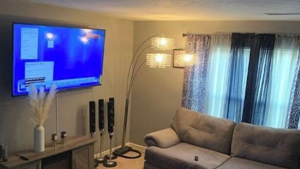 Ein Wohnzimmer mit Flachbildfernseher, grauem Sofa, Stehlampe und einem Vorhangfenster.