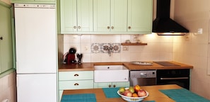 A kitchen with light green cabinets, a white refrigerator, a dishwasher, a stove, and a countertop with a fruit bowl.