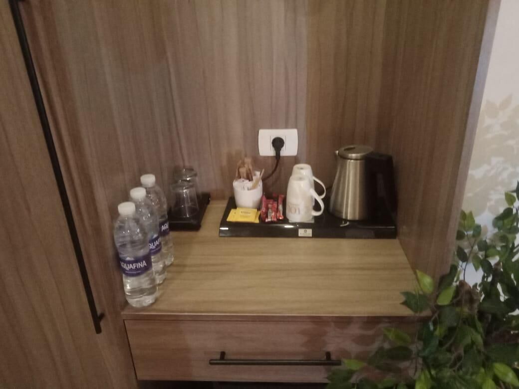 A wooden cabinet with a shelf containing a white mug, a stainless steel coffee pot, and a small white container. There are also three bottles of Aquafina water on the left side.