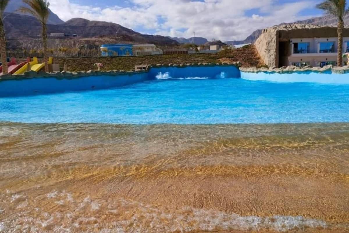 A pool with clear blue water, a sandy beach, and a mountainous backdrop.