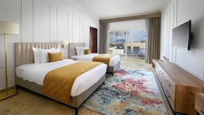 A hotel room with two beds, a large window with a view of the beach, a flat-screen TV, and a wooden dresser.