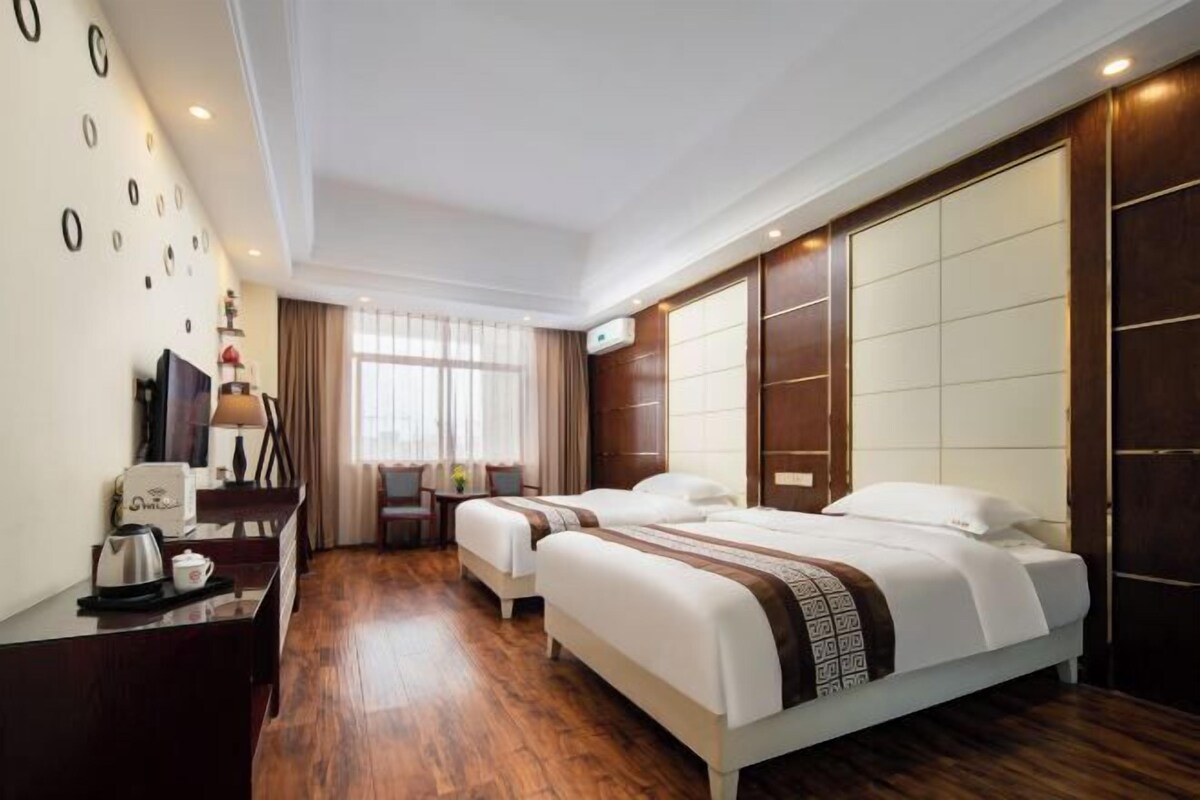 Een hotelkamer met twee bedden, een bureau met koffiezetapparaat, een televisie en een groot raam met gordijnen.