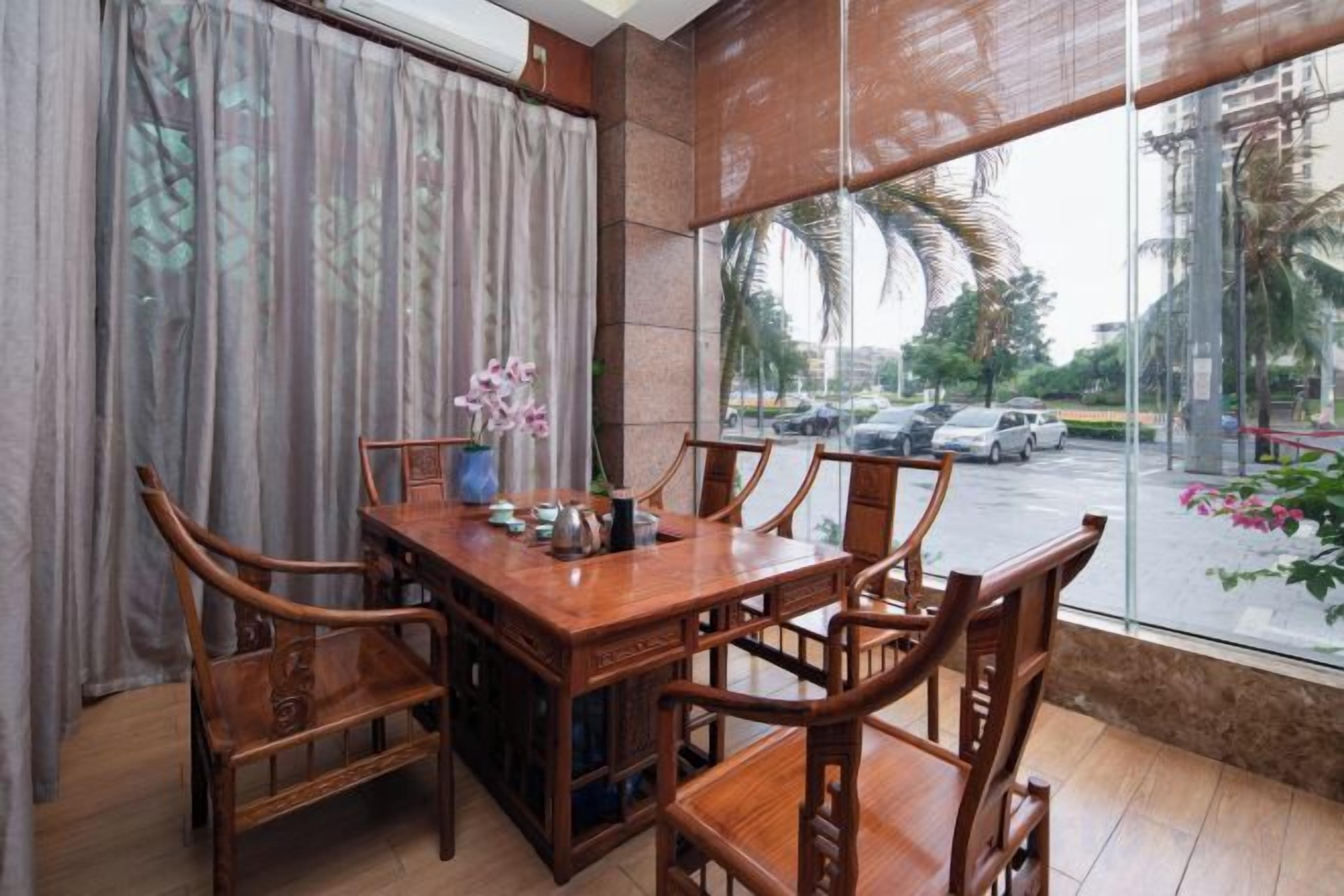 Un comedor con una mesa y sillas de madera, una ventana con vista a la calle y una cortina entreabierta.