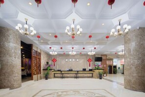Un vestíbulo de hotel con mostrador de recepción, candelabros y un techo decorativo.