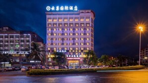 A multi-story hotel with illuminated signage, a parking lot, and surrounding buildings. - Yunchao International Hotel Danzhou (Danzhou)