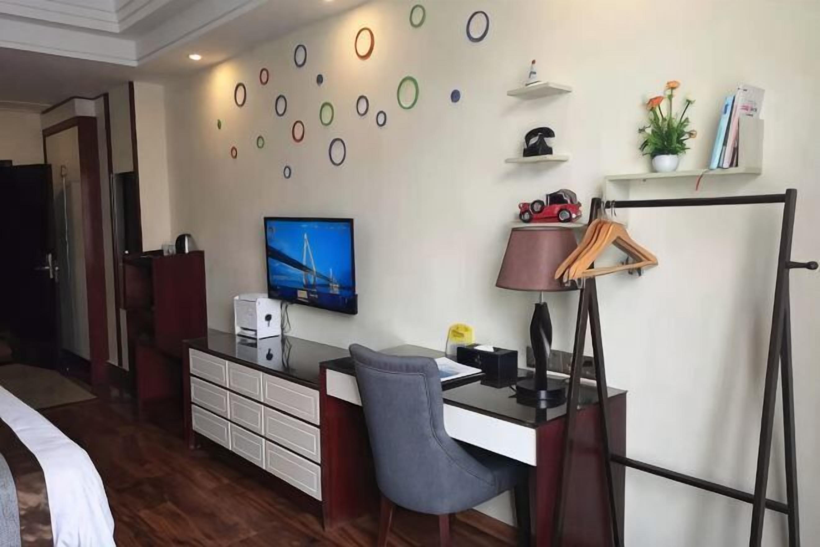 Una habitación de hotel con una cama, un escritorio con una silla, un televisor, una lámpara de escritorio, un perchero y una pared decorada con adornos circulares.
