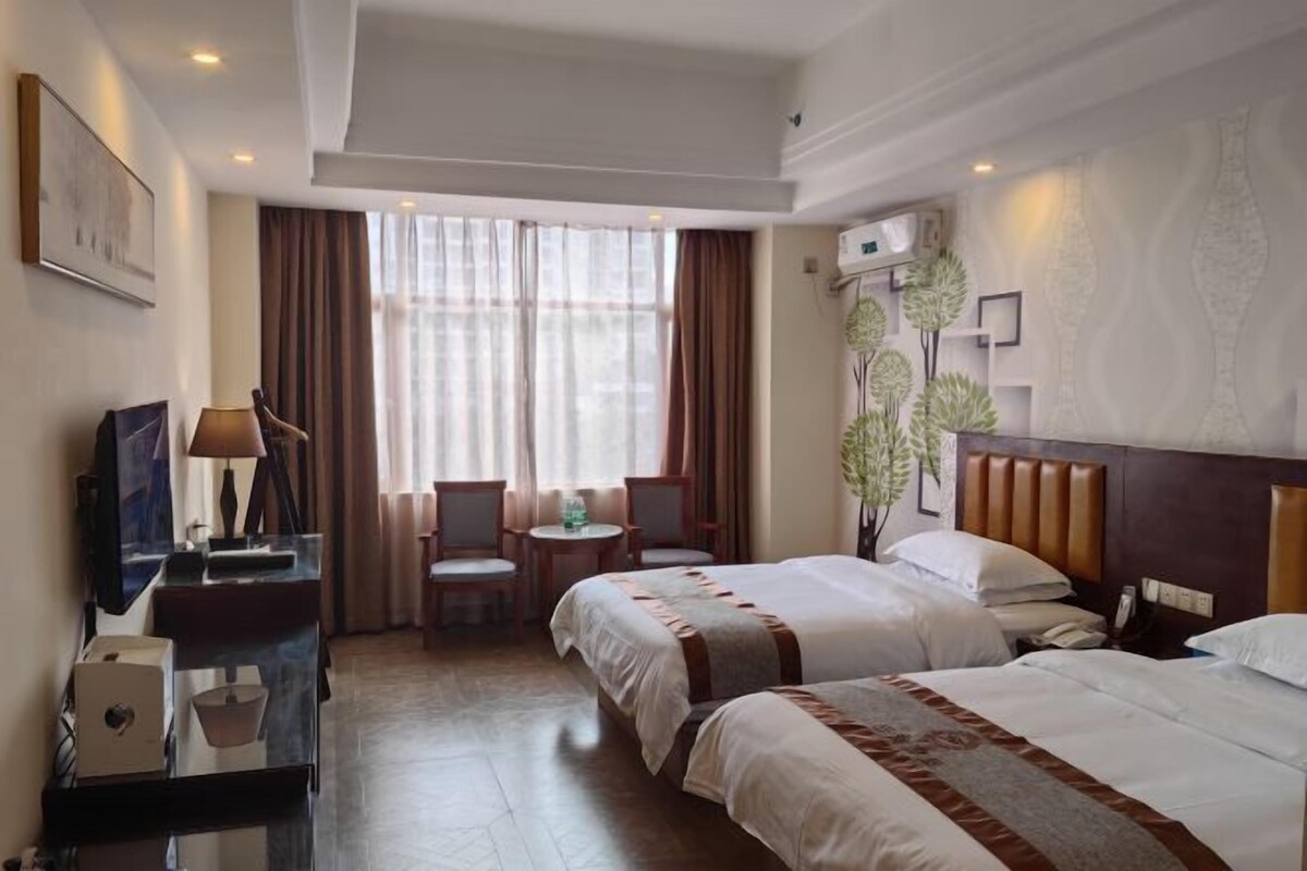 Een hotelkamer met twee bedden, een bureau met lamp, een kleine tafel met stoelen en een groot raam met gordijnen.