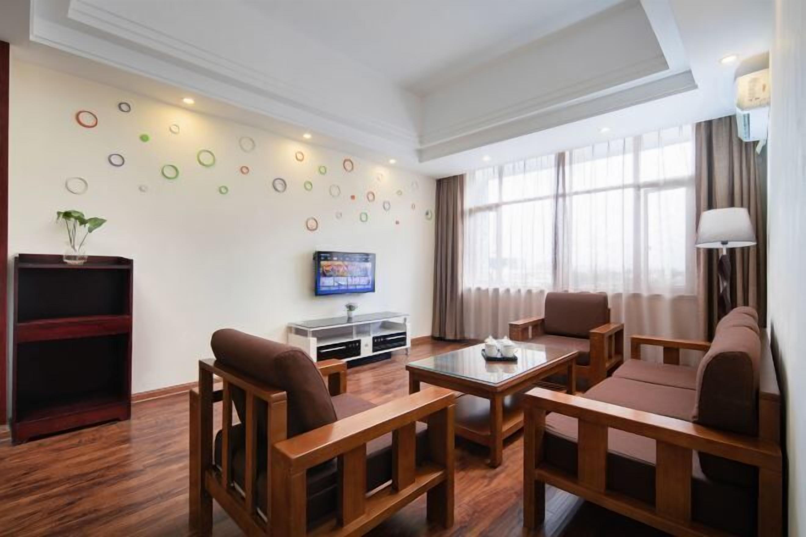 A hotel room with a wooden floor, a TV, a sofa, a coffee table, and a bookshelf.