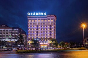 Un hotel de varios pisos con un letrero llamativo en la parte superior, un frente bien iluminado y un estacionamiento al frente.